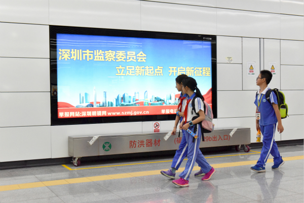 幾名學(xué)生邊走邊看福田地鐵站里深圳市監(jiān)察委員會的公益廣告